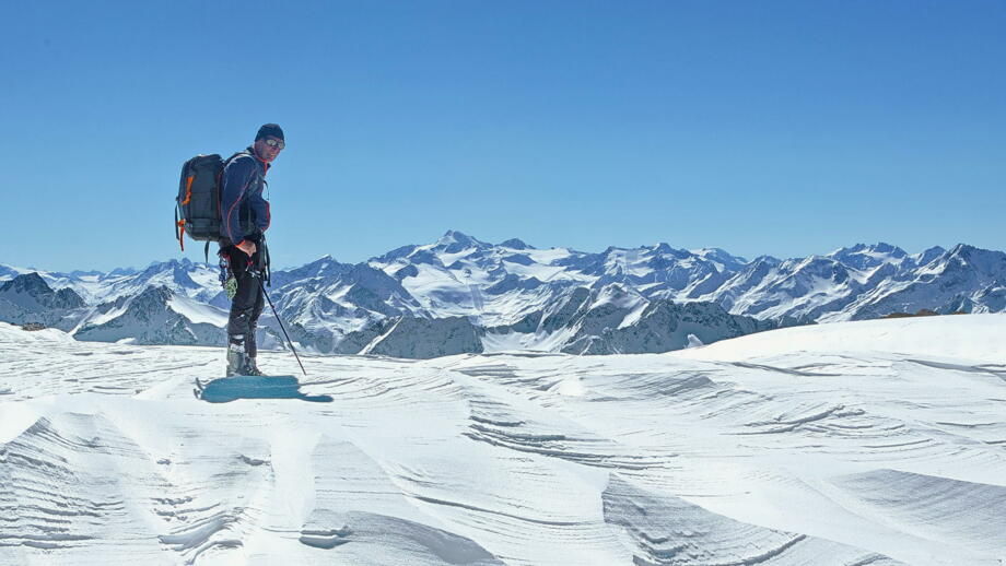 Skitourengeher bei Schneeverwehungen und blauem Himmel mit Aussicht