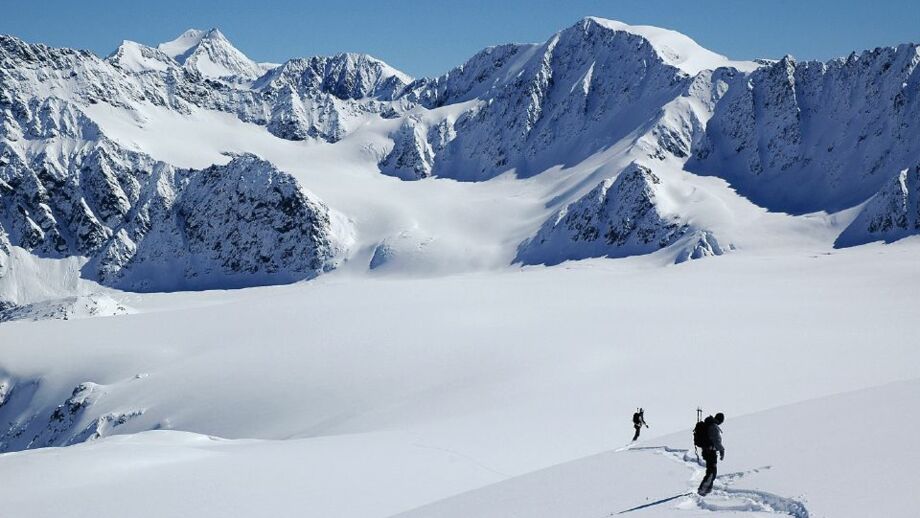 Zwei Skifahrer im unverspurten Tiefschneehang bei Gipfelkuliss