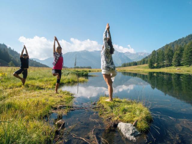 Drei Menschen beim Yoga an einem Fluss im Val di Sole