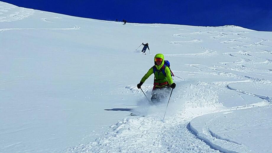 Skifahrer bei der Abfahrt im Tiefschnee mit blauem Himmel