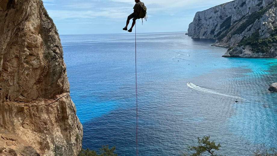 Wanderer beim Abseilen von einer Steilen Klippe, im Hintergrund das schöne blaue Meer mit einer Berglandschaft