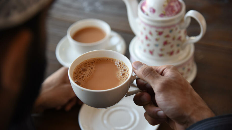Hand hält Teetasse und weiteres Teegeschirr