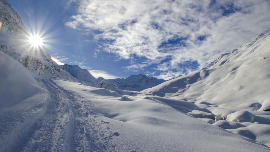 Sonnenstrahlen scheinen in einen verschneiten Aufstiegshang im Sellrain