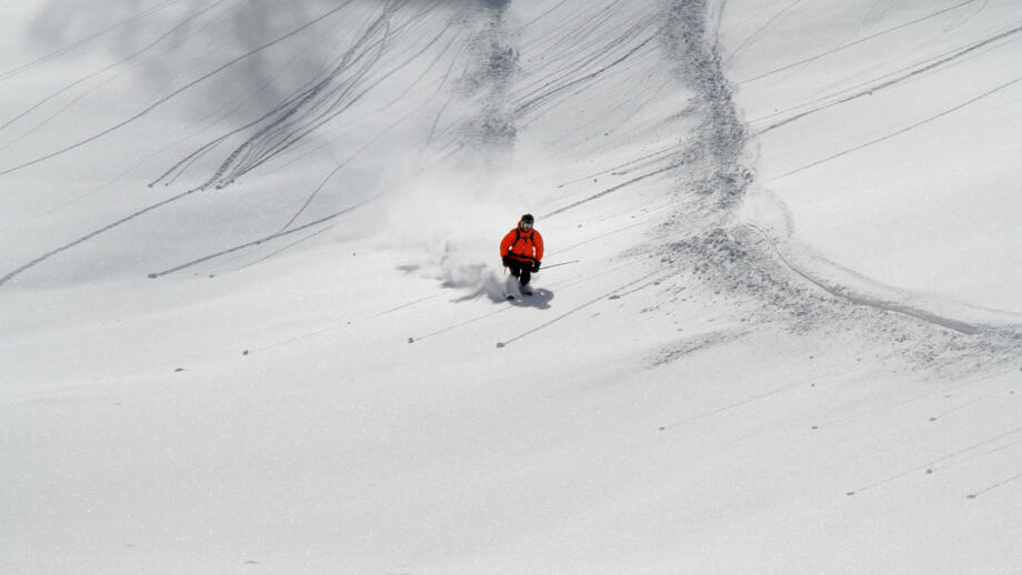 Tiefschneefahrer mit roter Jacke zieht seine Spuren im Powder