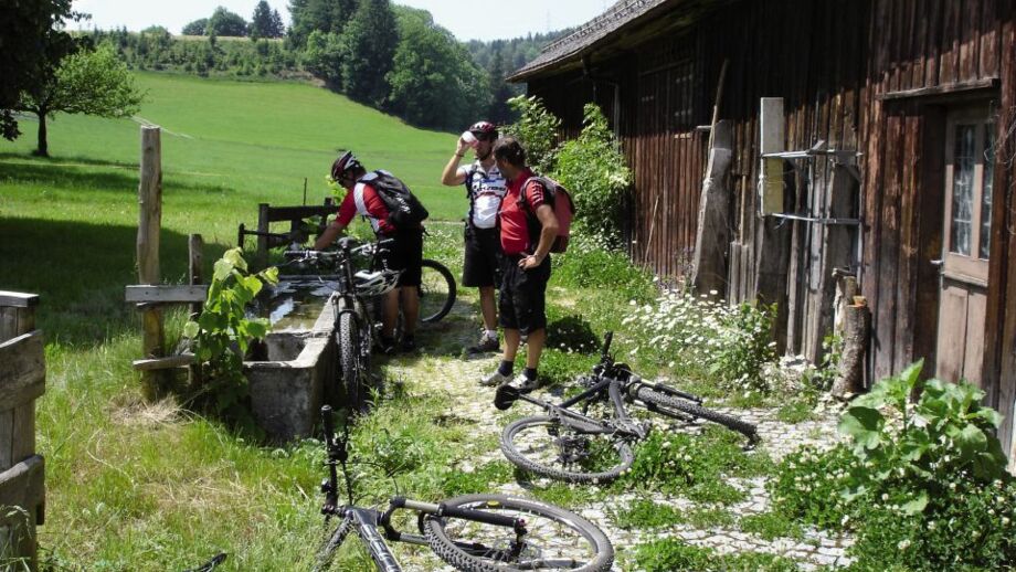 Eine Mountainbike Gruppe bei der wohlverdienten Pause während der Tour durch die Schweiz an einer Almhütte bei sonnigem Wetter.
