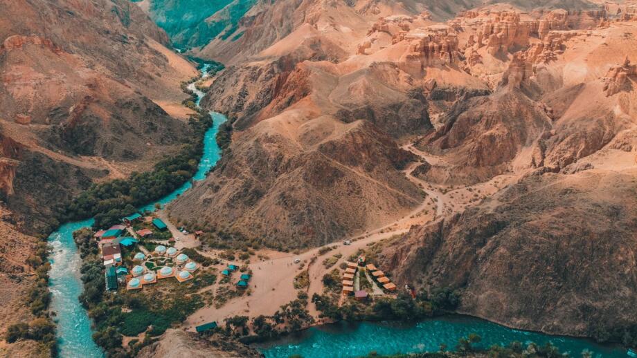 Blick in den Charyn-Canyon von Oben mit Fluss, buntem Zeltlager und schroffen Felsen rundum