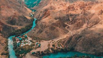 Blick in den Charyn-Canyon von Oben mit Fluss, buntem Zeltlager und schroffen Felsen rundum