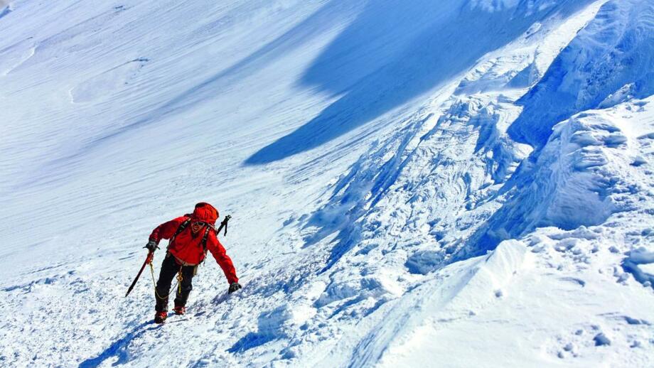 Bergsteiger mit roter Jacke, Pickel und Steigeisen bei der Querung einer Schneeflanke am Fünftausender Kasbek in Georgien
