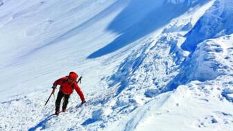 Bergsteiger mit roter Jacke, Pickel und Steigeisen bei der Querung einer Schneeflanke am Fünftausender Kasbek in Georgien
