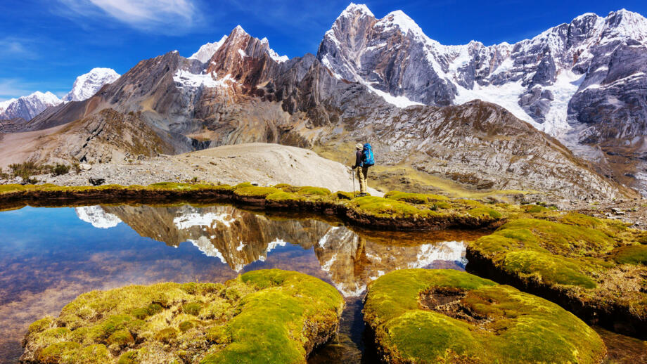 wanderer an einem Bergswee, in dem sich die umliegenden Gipfel spiegeln