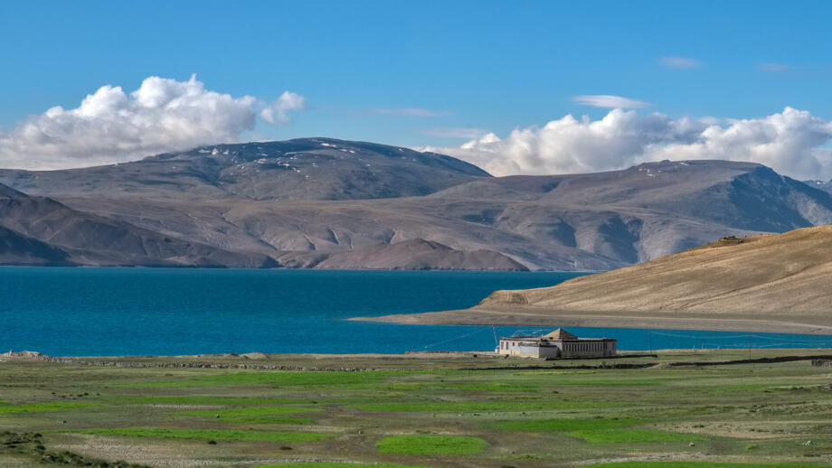 Buddhistisches Kloster auf blauen Moririsee mit grüner Wiese im Vorder- und Bergkette im Hintergrund