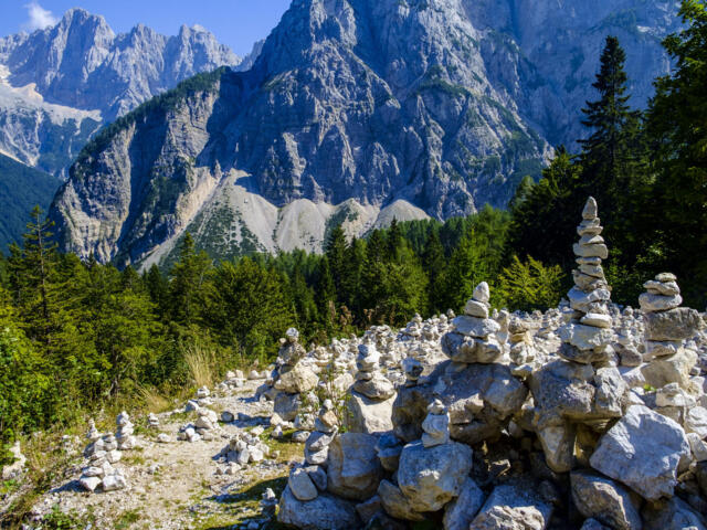 Die gebauten Steinmännchen in den slowenischen Bergen mit der Gipfelwelt im Hintergrund bei Sonnenschein.