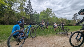 Ein Gruppe an Mountainbiker*innen, die auf einer Wiese mit Ihrem Mountainbike stehen und gemeinsam den Bike-Check durchführen.