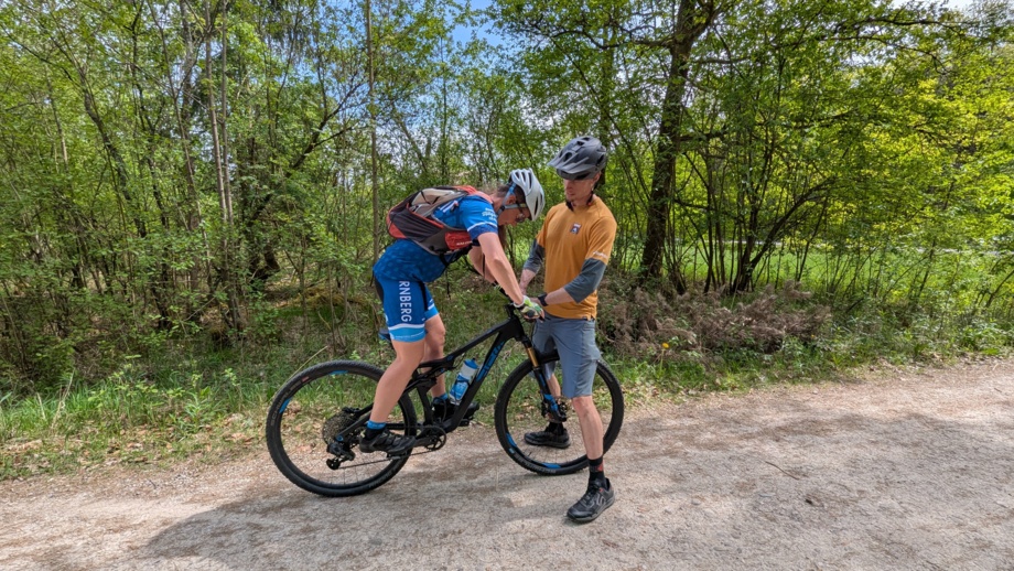 Eine Mountainbiker*in auf einer Forststraße mit Ihrem Bike Guide bei einer Gleichgewichtsübung während des MTB-Fahrtechniktrainings.