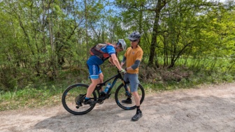 Eine Mountainbiker*in auf einer Forststraße mit Ihrem Bike Guide bei einer Gleichgewichtsübung während des MTB-Fahrtechniktrainings.