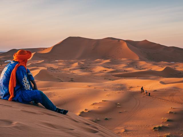 Beduine sitzt auf Düne und Blick in den Sonnenuntergang