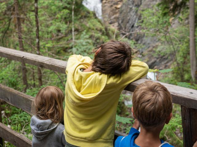 Drei Kinder lehnen an einen Holzzaun und schaun auf den Martuljek Wasserfall