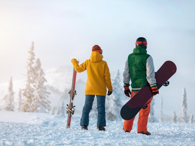 Skifahrer und Snoboarder nebeneinander in verschneiter Landschaft