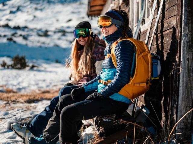 Zwei Wintersportler*innen sitzen auf der Bank