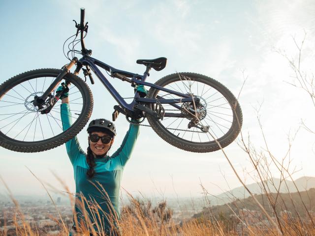 Radfahrerin hält ihr Fahrrad über den Kopf und jubelt
