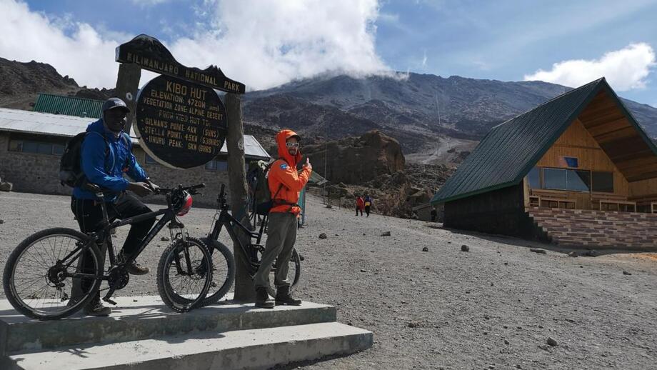 Eine Gruppe von Mountainbiker auf Ihrem Weg zum Gipfel des Kilimandscharos. Sie stehen am Schild der Kibo-Hütte. Ein Zwischenziel.