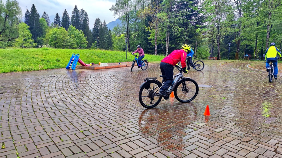 Eine Gruppe an E-Mountainbiker auf einem gepflasterten Platz bei leichten Regen während einer E-MTB Fahrtechnik-Trainingsübung.