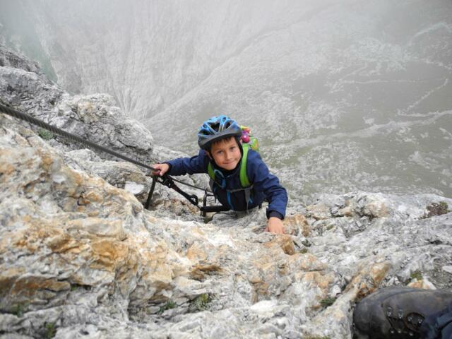 Junge auf einem Klettersteig im Nebel