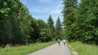 Zwei Fahrradfahrer fahren auf einer Straße durch den Perlacher Forst.