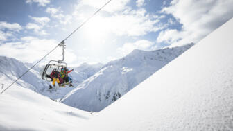 Skifahrer im Sessellift mit Schnee im Vordergrund