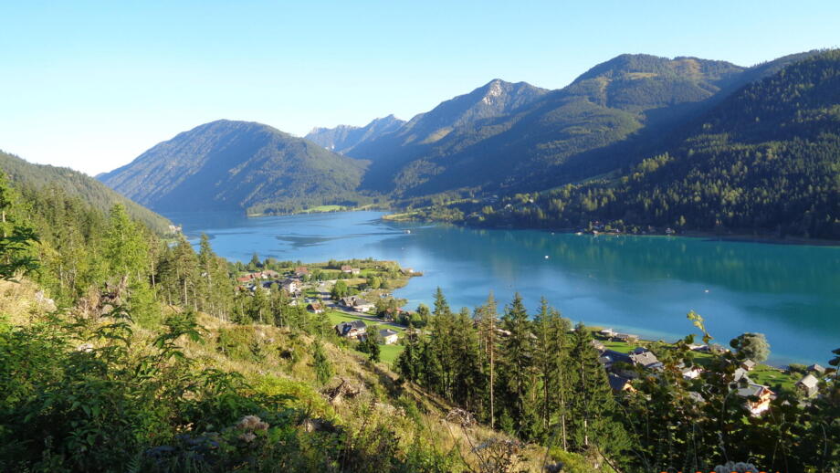 Der Weissensee - ein Highlight der E-MTB Transalp. Um den See erheben sich die Berge. Die Sonne scheint.