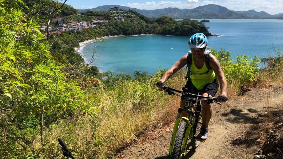 Ein Mountainbikerin in Costa Rica auf einem Trail. Im Hintergrund sieht man das Meer.