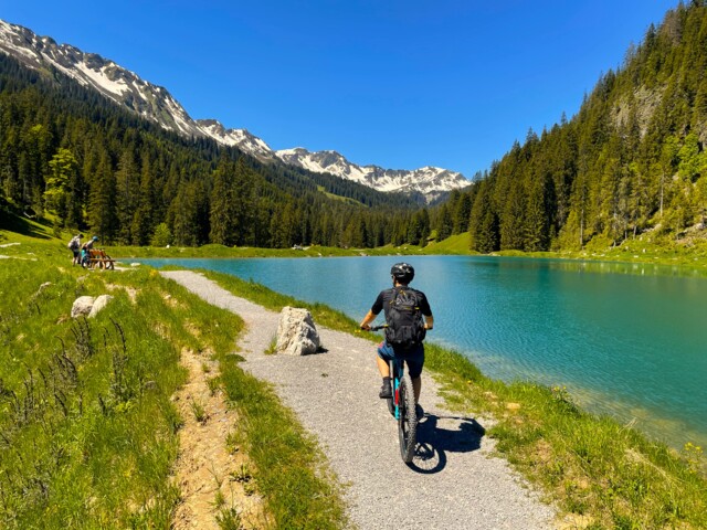 Biker unterwegs am Herzsee im Kleinwalsertal. Die Sonne scheint. Der Himmel ist blau.
