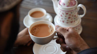 Hand hält Teetasse und weiteres Geschirr