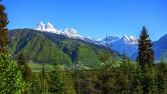 Dorf Ananuri in Swanetien in grünem Bergland mit vergletscherten Kaukasus-Gipfeln im Hintergrund