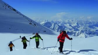 Gruppe von Skibergsteigern im winterlichen Aufstieg zum Fünftausender Kasbek mit Blick auf weitere schneebedeckte Kaukasus-Gipfel