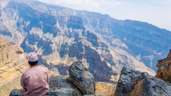 Omaner sitzt an einem Ausguck  und blickt auf das karge Hadschar-Gebirge