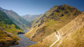 Wanderer hoch über dem Flusstal im Aufstieg entlang der Berghänge zum Atsunta-Pass in Tuschetien, Georgien