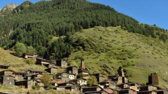 Dorf mit Wohnhäusern und Wehrtürmen in grüner Gras- und Baumlandschaft in Chewsuretien, Georgien