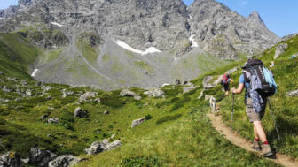 Zwei Bergwandernde mit Hund in grüner Almlandschaft vor felsiger Bergkulisse in Georgien