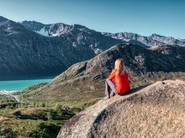 Eine Frau blickt an einem sonnigen Tag auf den Gjende-See im Jotunheimen Nationalpark