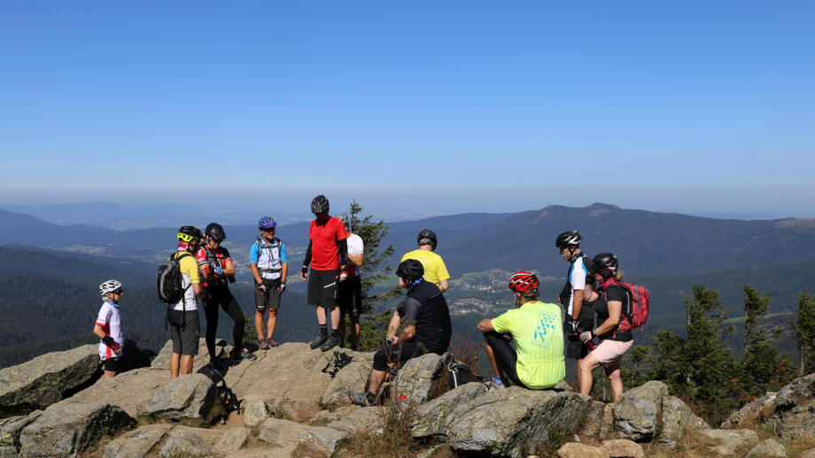 Eine Gruppe während der Trans Bayer Wald auf einem Gipfel der Berge des Bayerischen Walds. Die Gruppe genießt die Fernsicht. Der Himmel ist blau und die Sonne scheint.