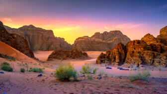 Lager mt blauen Zelten im Wadi Rum mit Sand, Felsen und grrünen Büschen