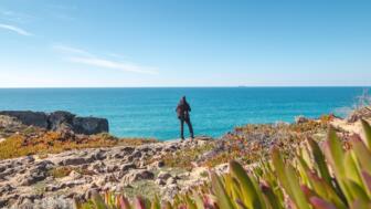 Wanderer mit Blick auf das Meer von Felsklippen bei Vila Nova de Milfontes