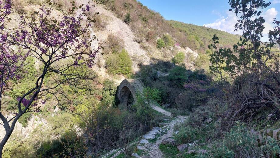 Ein schmaler Wanderpfad im Süden Albaniens der im weiteren Verklauf über eine steinerne Brücke führt