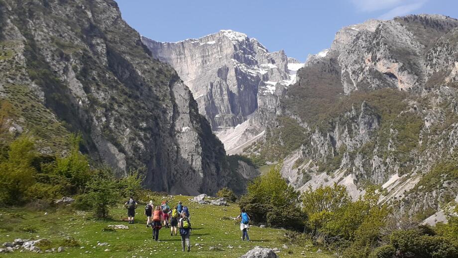 Eine Wandergruppe läuft über Wiesen umgeben von hohen Felswänden im Süden Albaniens