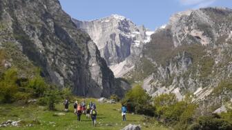 Eine Wandergruppe läuft über Wiesen umgeben von hohen Felswänden im Süden Albaniens