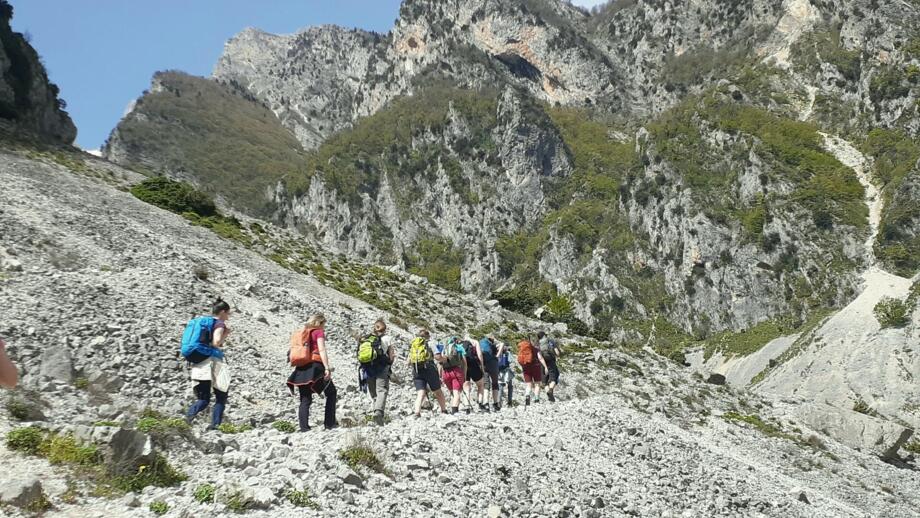 Eine Wandergruppe passiert einen schmalen Pfad umgeben von felsigen Wänden