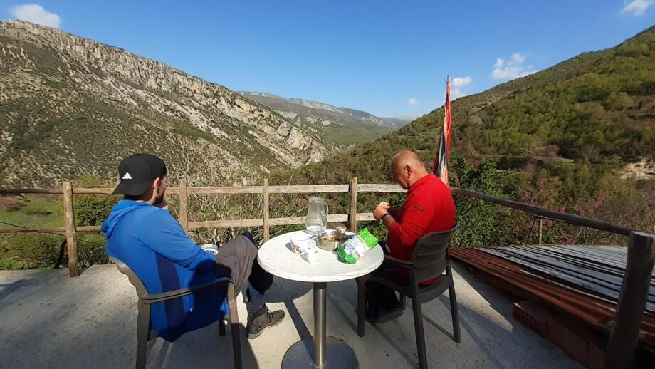 Zwei Menschen an einem runden Tisch, die auf die bergige Landschaft im Süden Albaniens schauen