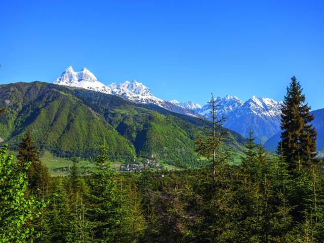 Wiesen, Dorf und Wälder vor vereisten Kaukasus-Gipfeln
