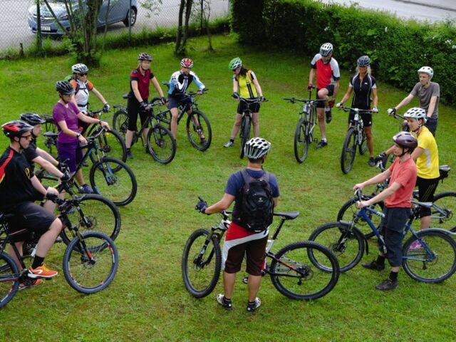 Mountainbiker*innen beim E-MTB Kontrollcheck auf einer Wiese vor Tourenstart